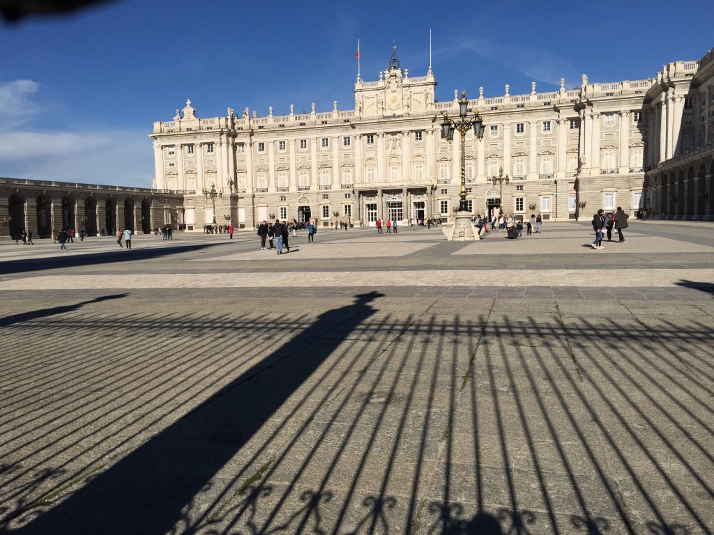 The Royal Palace of Madrid with a clear blue sky and shadows cast on the ground.
